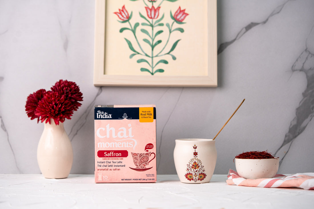 A box of Tea India Instant Saffron chai on a table along with a cup of chai and a bowl of saffron strands.