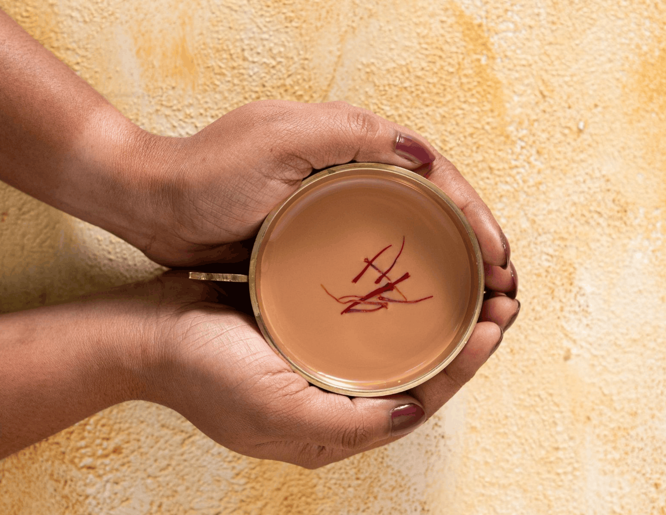 A girl holding a cup of Tea India Instant Saffron Chai with a few saffron strands in it