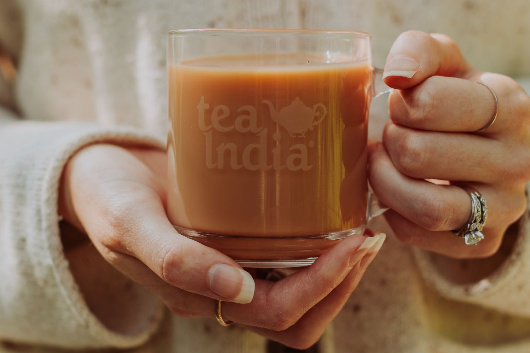 Hands holding a glass Tea India mug filled with milk tea.