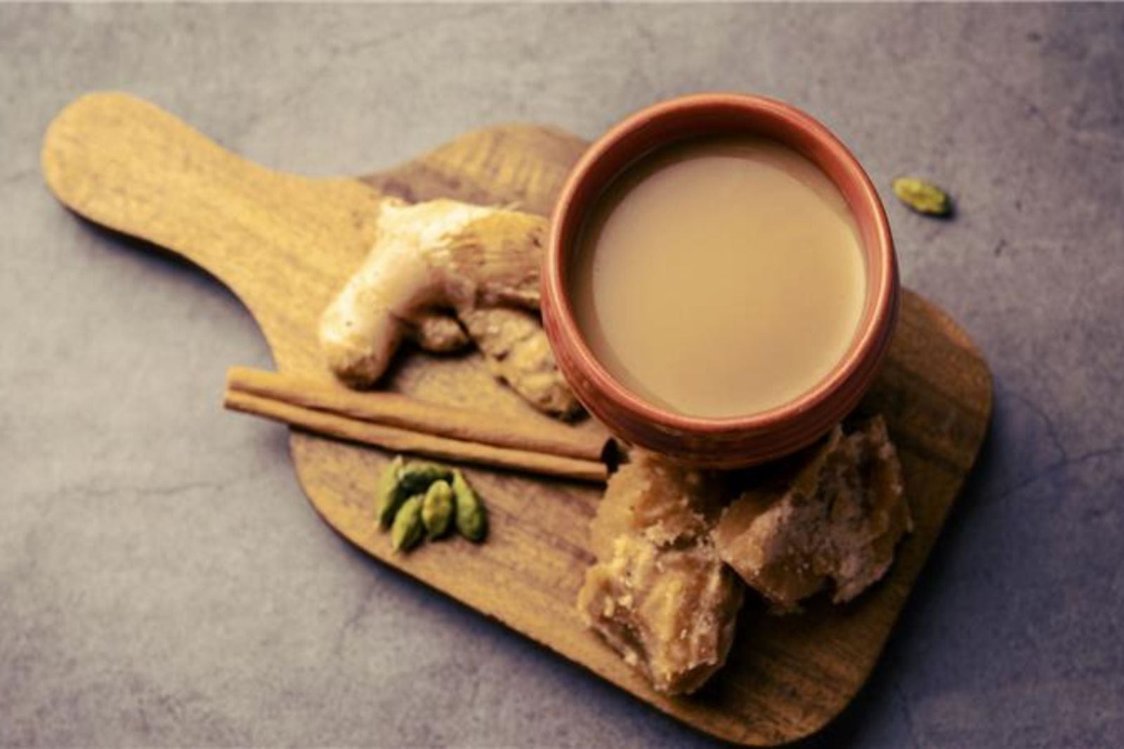 Clay cup of milky ginger tea served with cinnamon, cardamom, and jaggery.