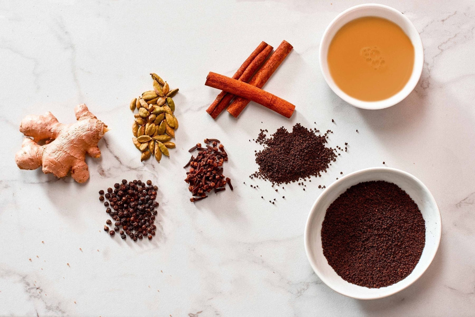 Overhead view of masala chai in a black cup surrounded by whole spices.