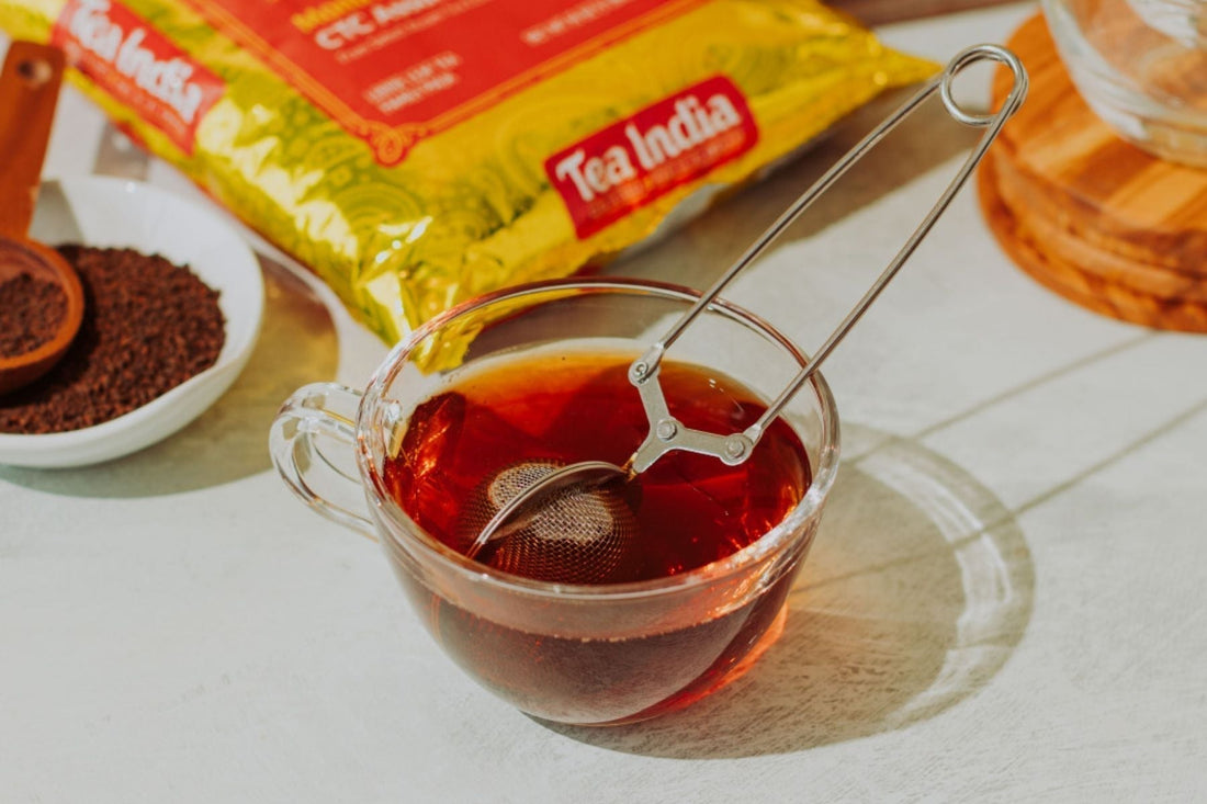 Infuser steeping in a mug of black chai tea near a jar of Tea India CTC loose tea