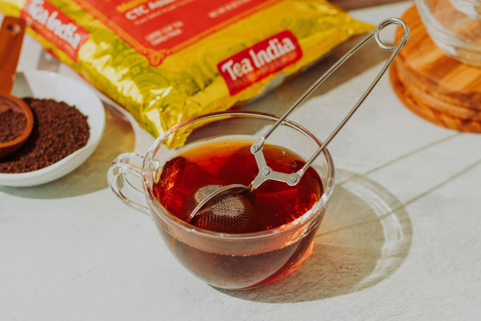 Infuser steeping in a mug of black chai tea near a jar of Tea India CTC loose tea