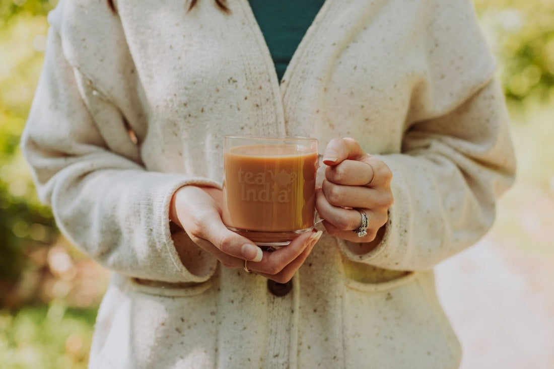 Person in a cream sweater holding a glass mug of tea outdoors