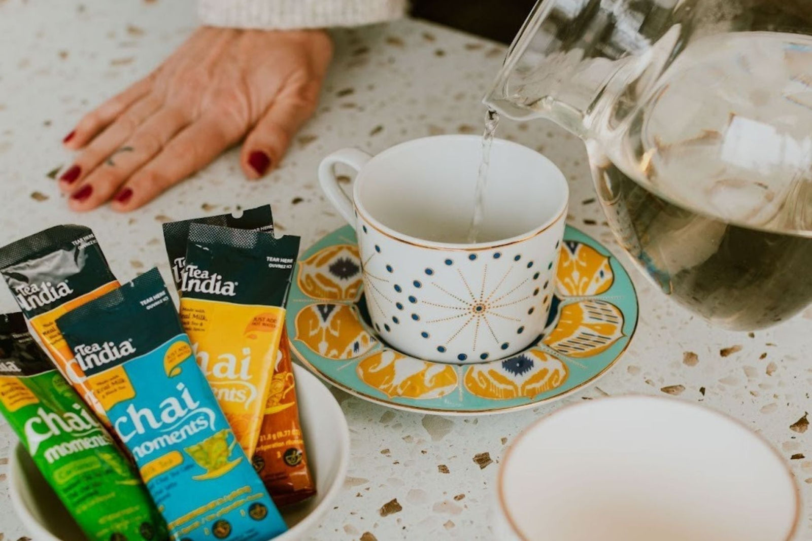 Warm water being poured into a cup alongside Tea India Instant Chai Mix