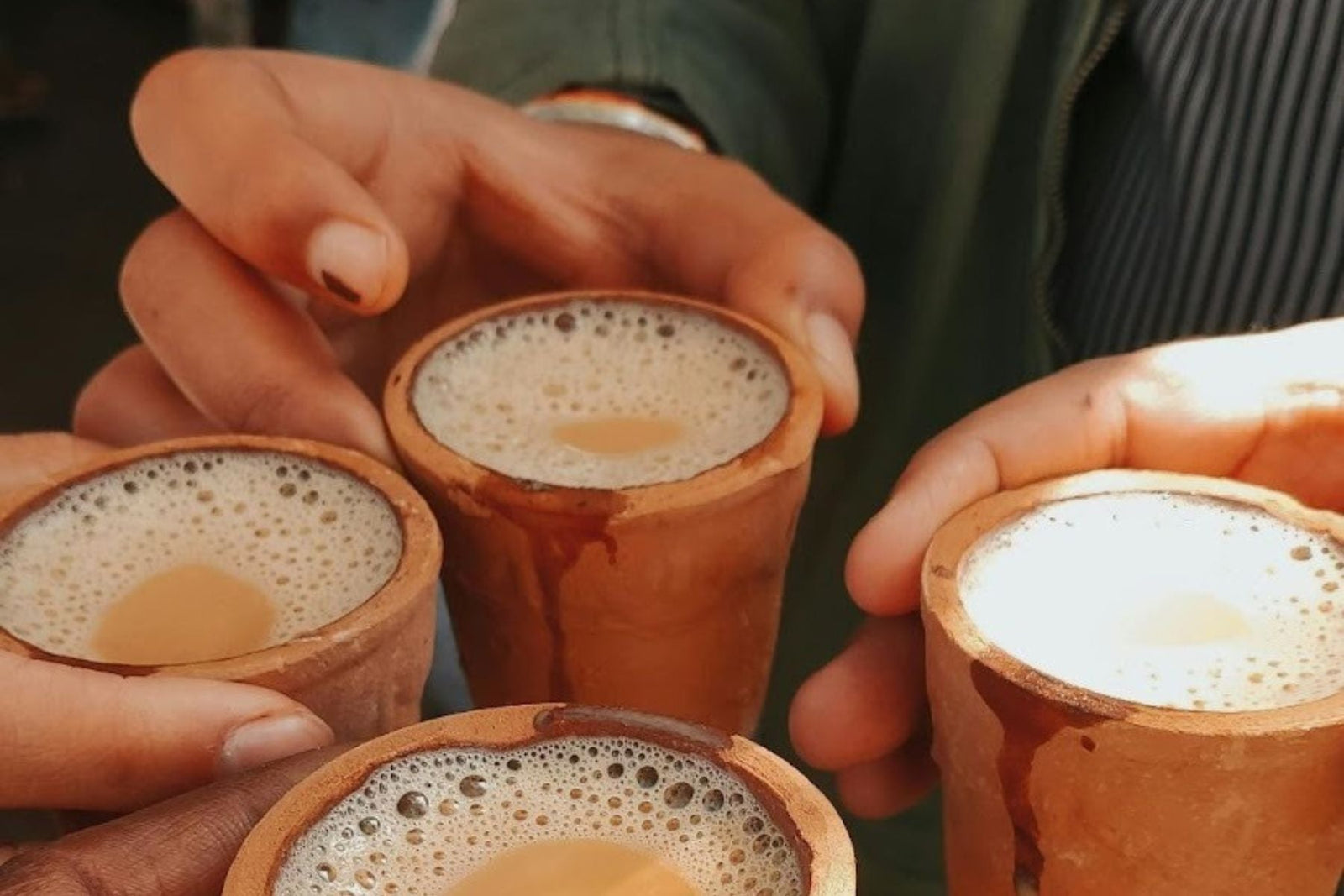 Four hands holding four cups of chai tea