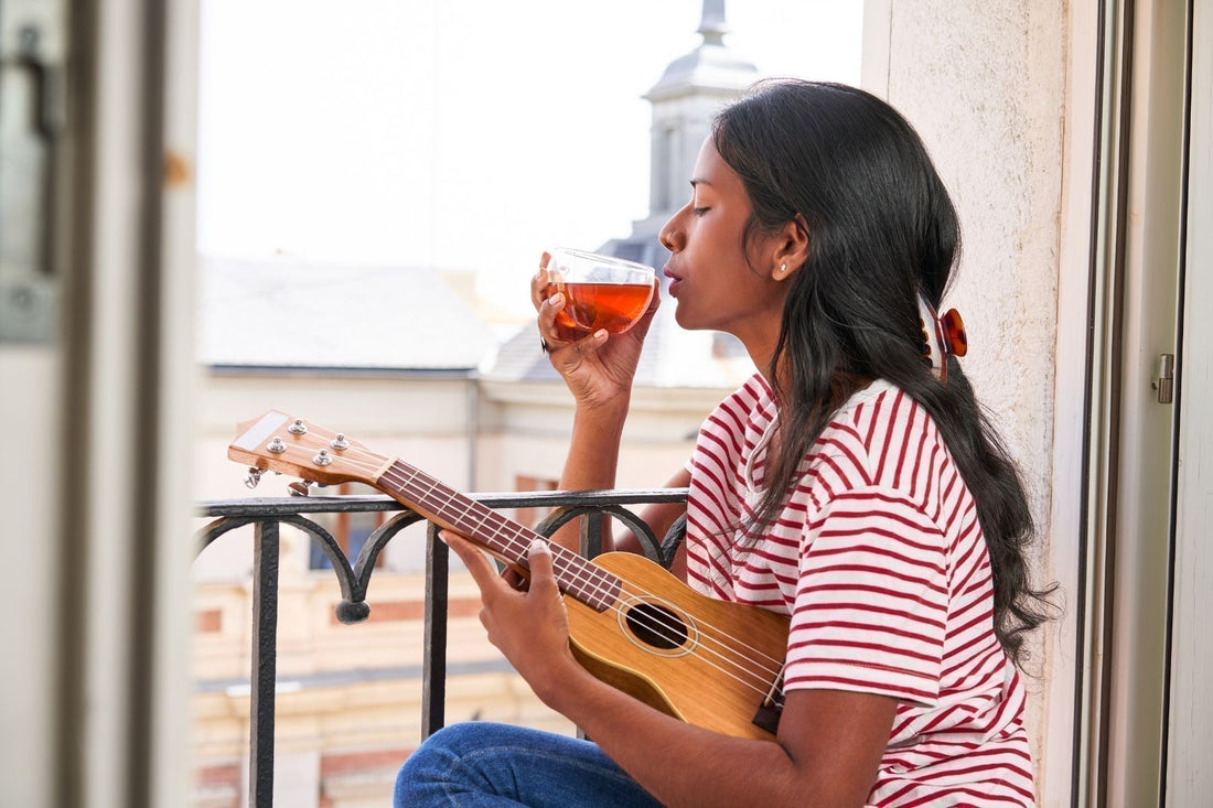 Woman on a balcony holding a glass of tea and a ukulele