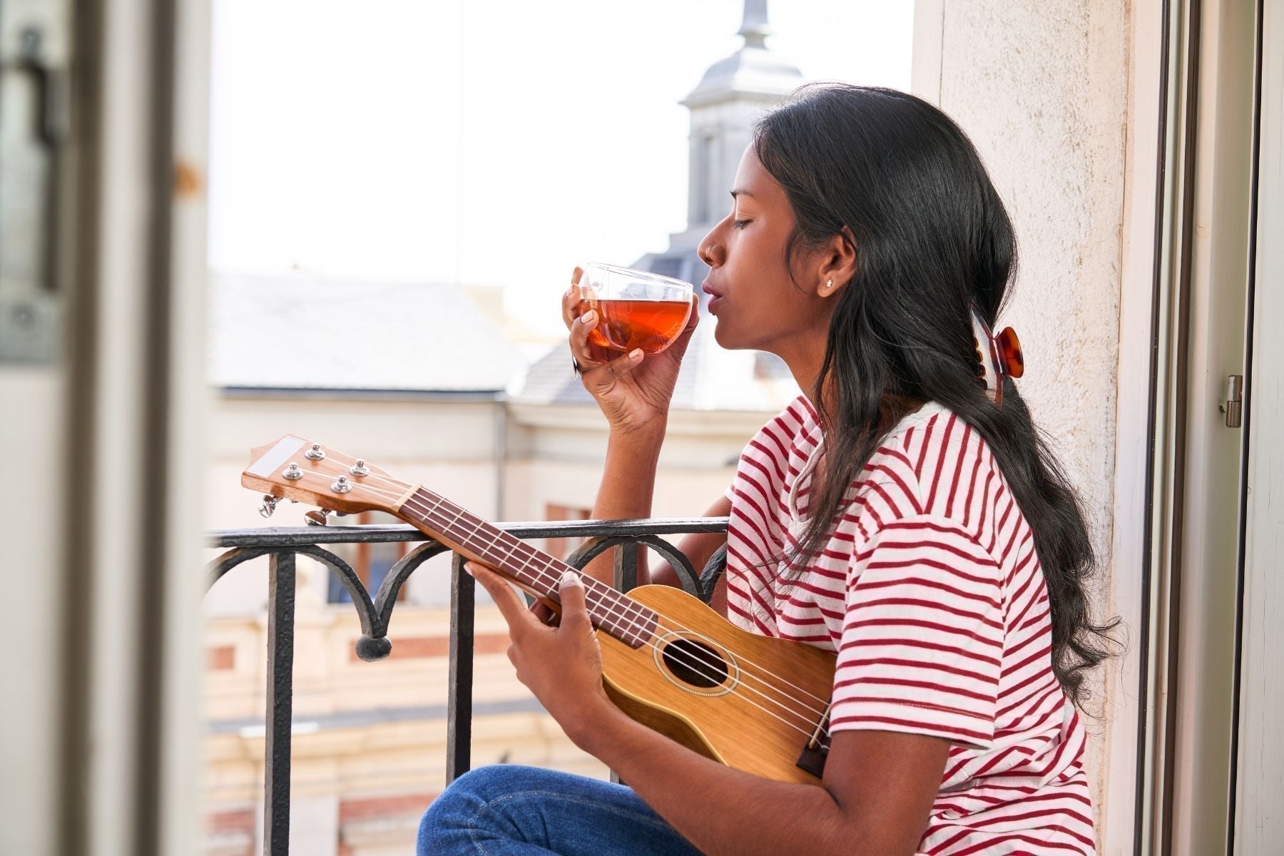 Woman on a balcony holding a glass of tea and a ukulele