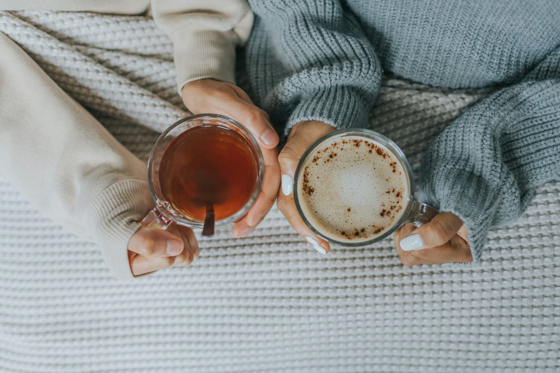 Two people holding cups of tea and coffee, relaxing together on a cozy blanket