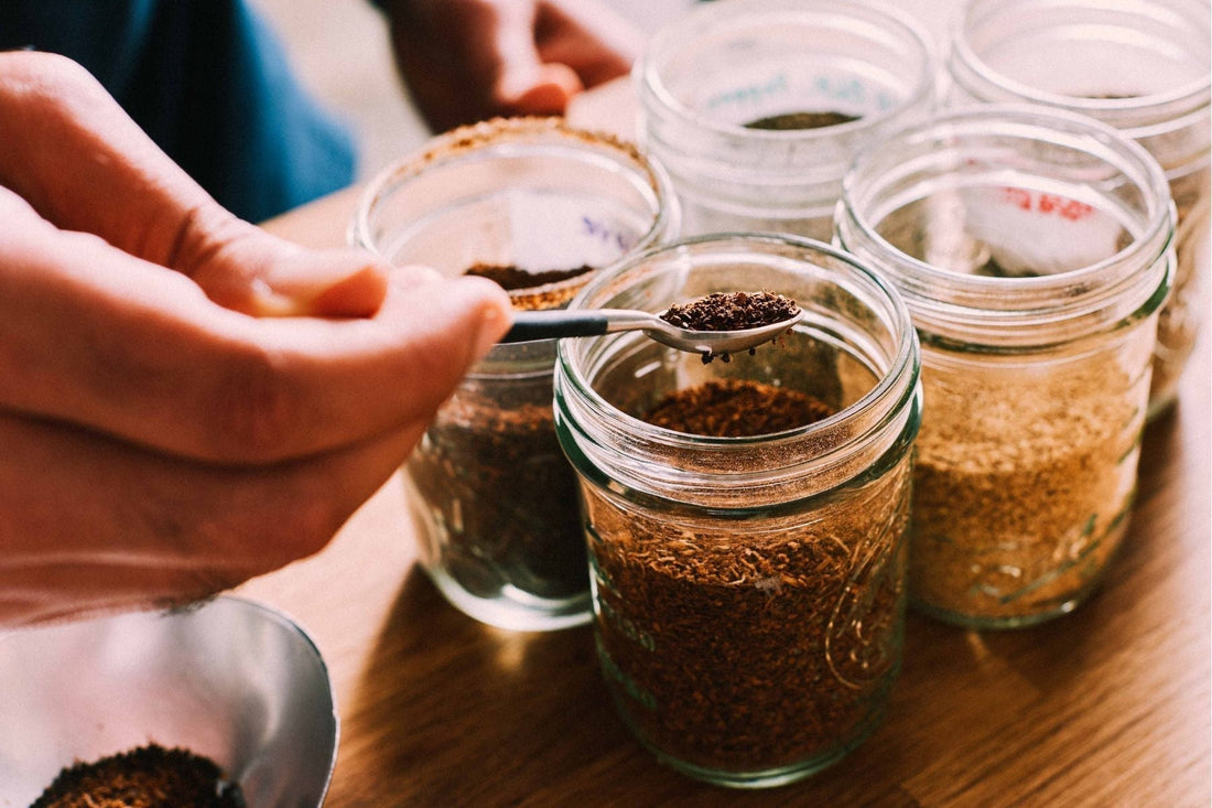 Scooping loose tea leaves and other spices from glass jars for blending or brewing