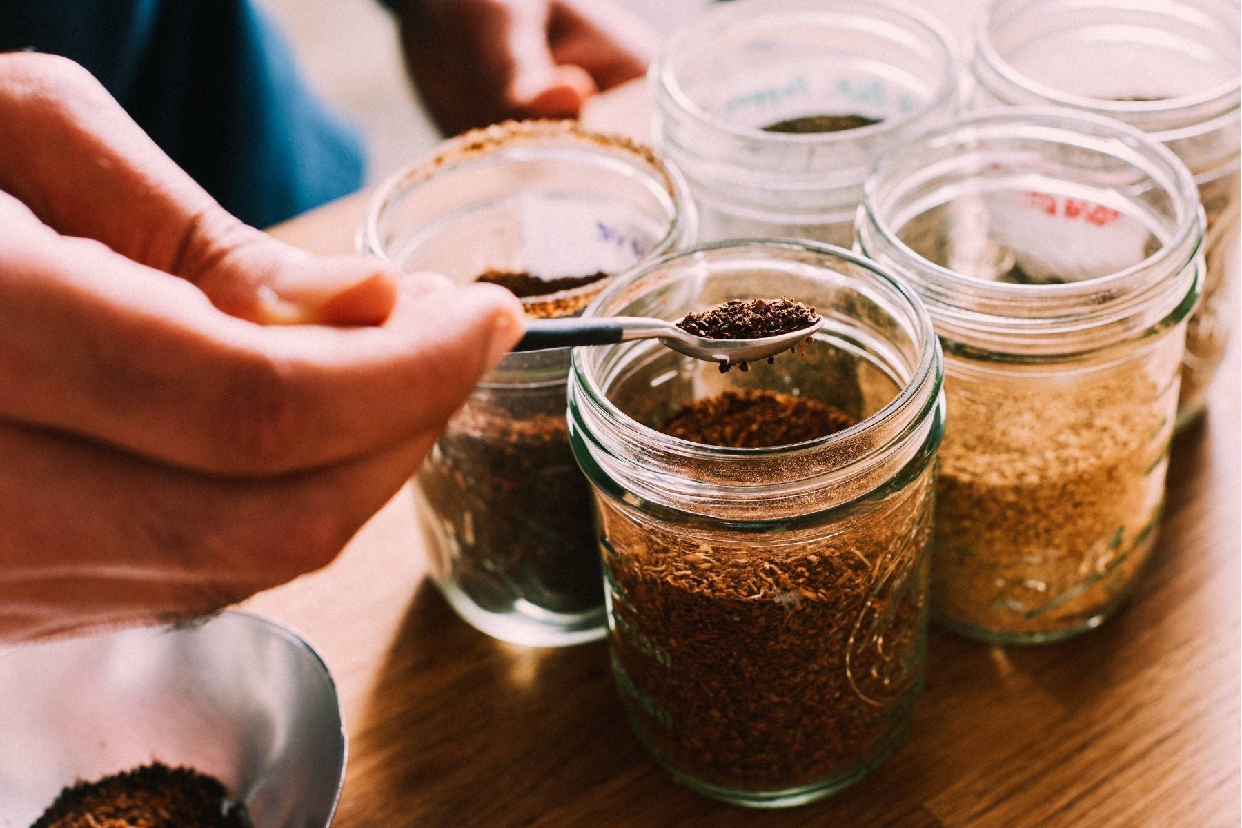 Scooping loose tea leaves and other spices from glass jars for blending or brewing