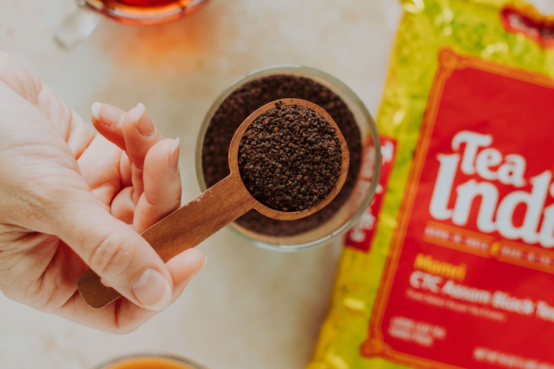 Measuring loose CTC Assam tea leaves with a wooden spoon beside Tea India pack