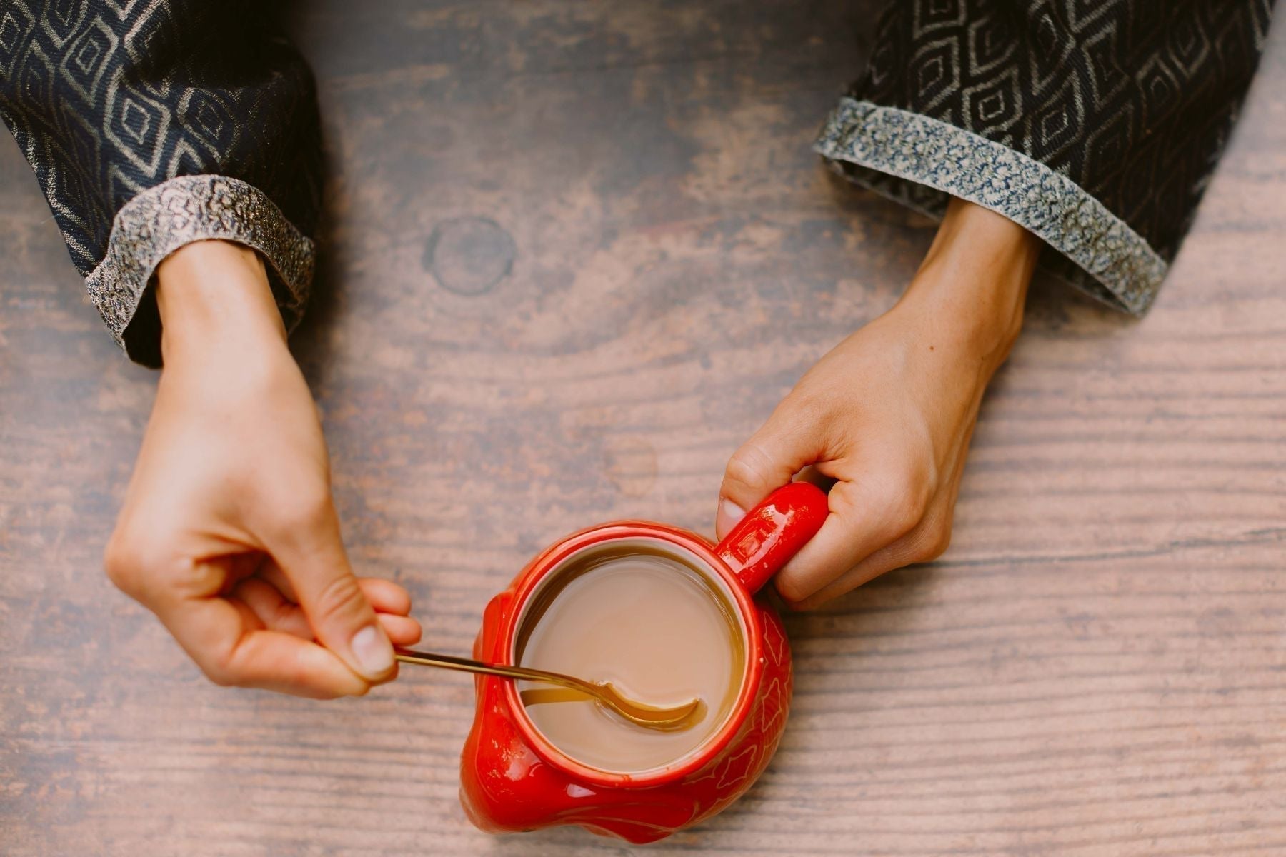 Hand stirring tea in a red cup on a wooden surface