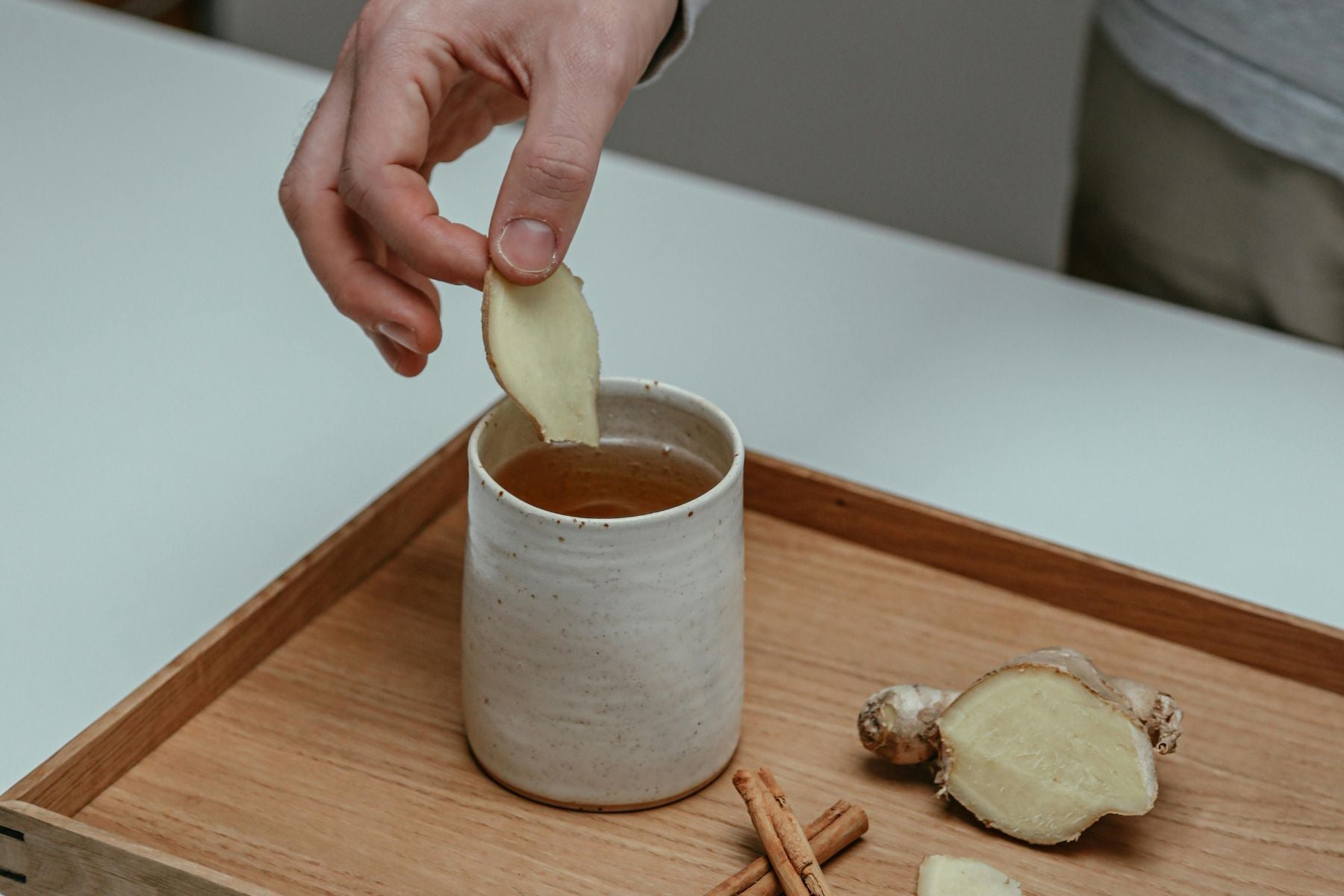 Hand adding a slice of ginger into a cup of tea
