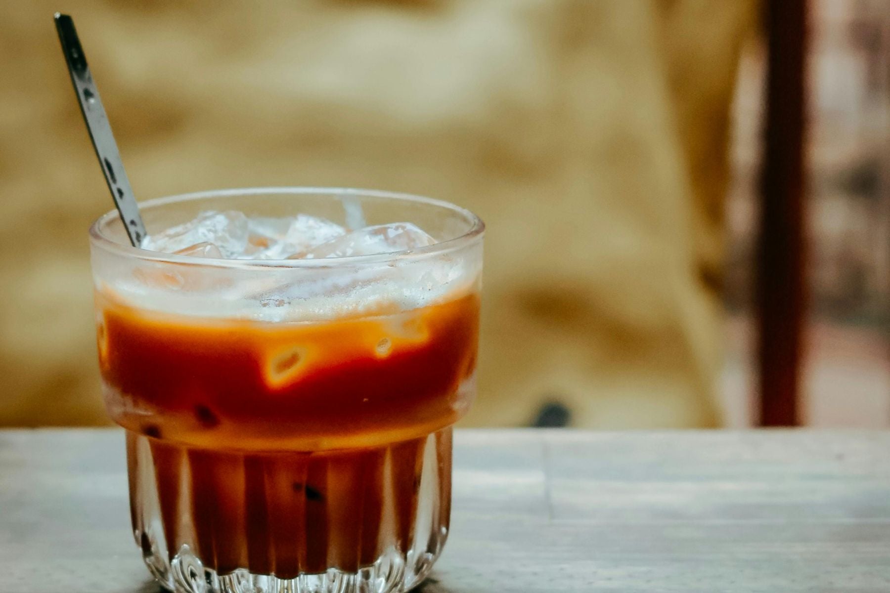 A glass of Vanilla Iced Chai Latte with ice cubes, showing rich amber tones and a creamy layer near the top.