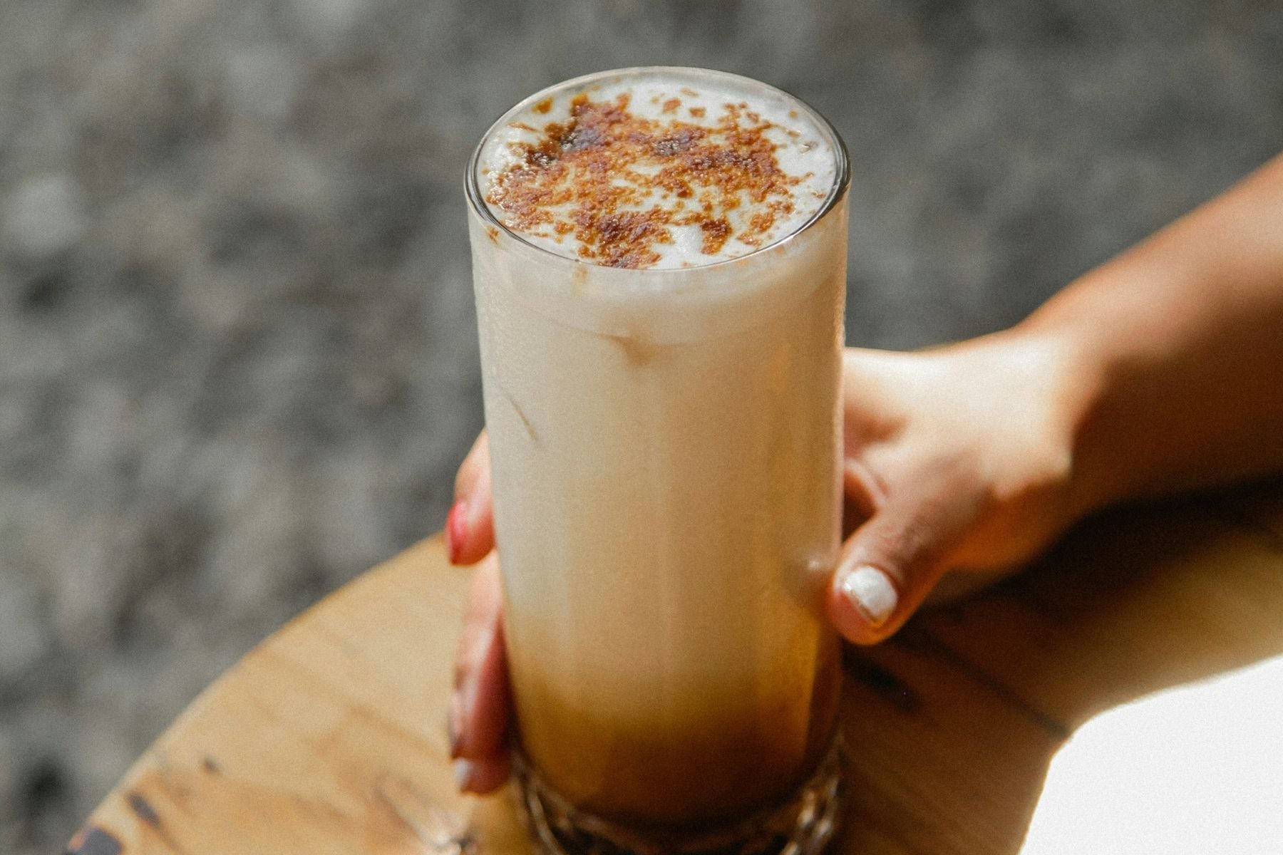 Hand holding a frothy Skinny Iced Chai Latte in a tall glass