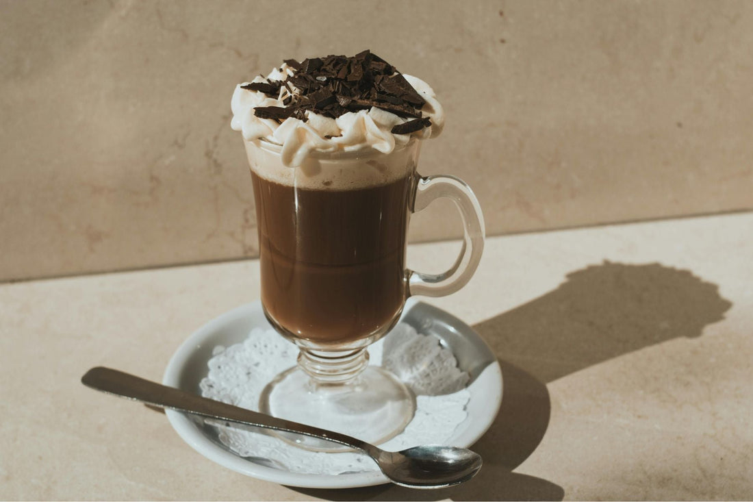 Glass mug of Chocolate Mocha topped with whipped cream and chocolate shavings on a saucer