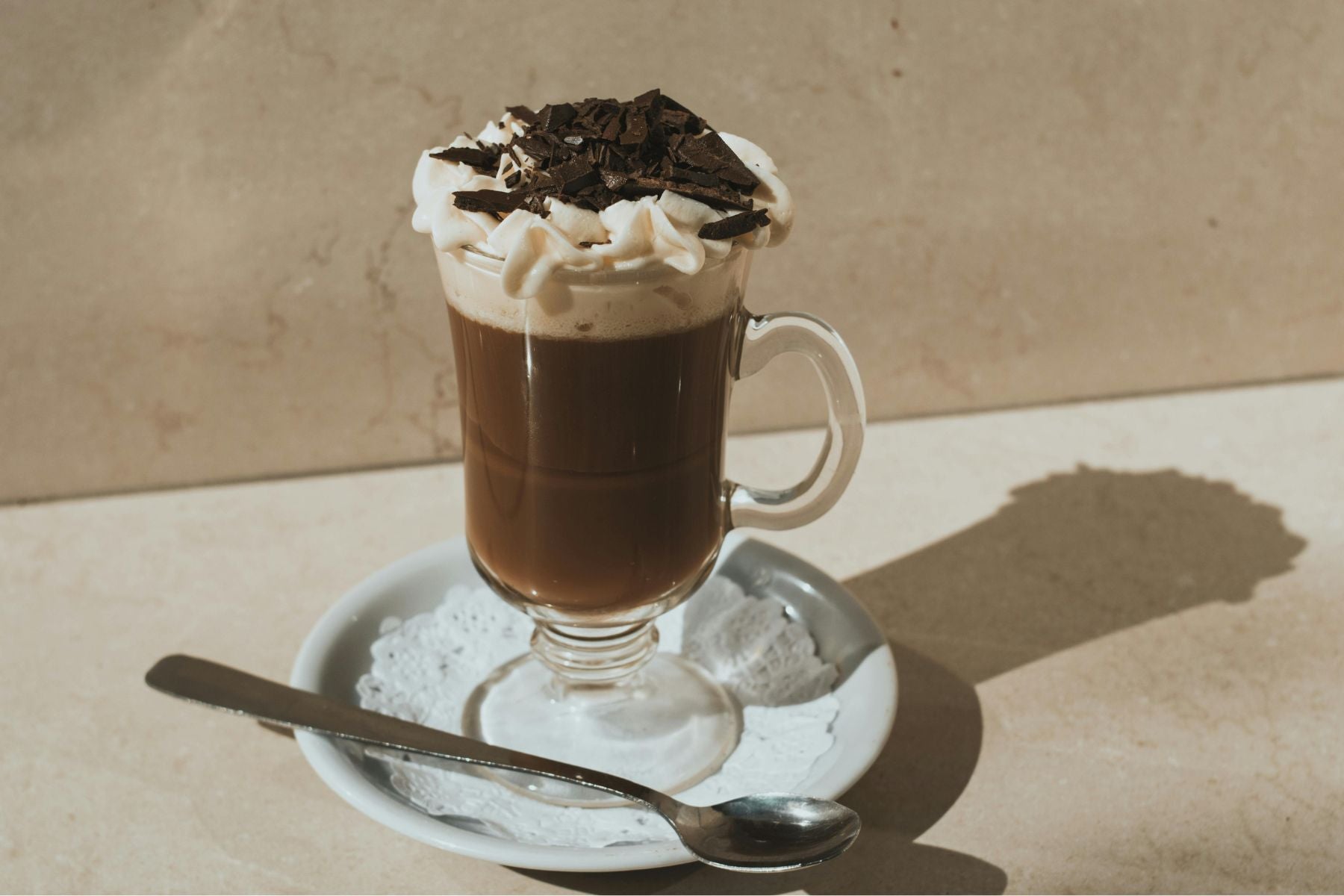 Glass mug of Chocolate Mocha topped with whipped cream and chocolate shavings on a saucer