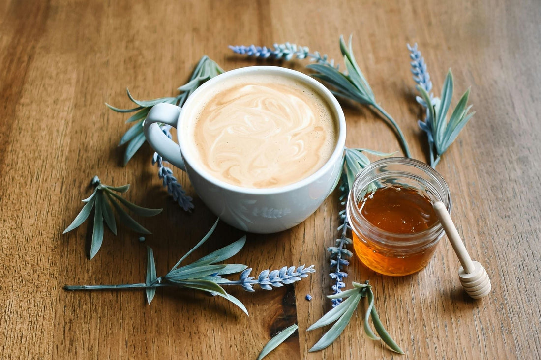 Cup of chai on a wooden table with lavender sprigs and a jar of honey beside it
