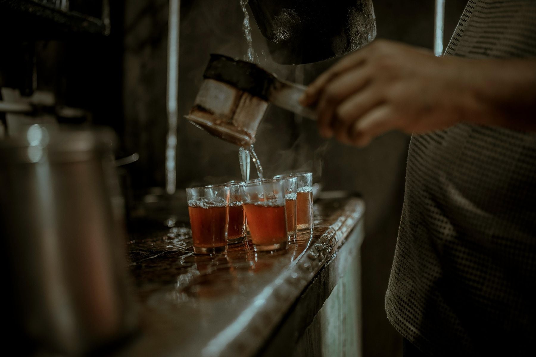 Tea being poured from a kettle into multiple small glass cups on a counter