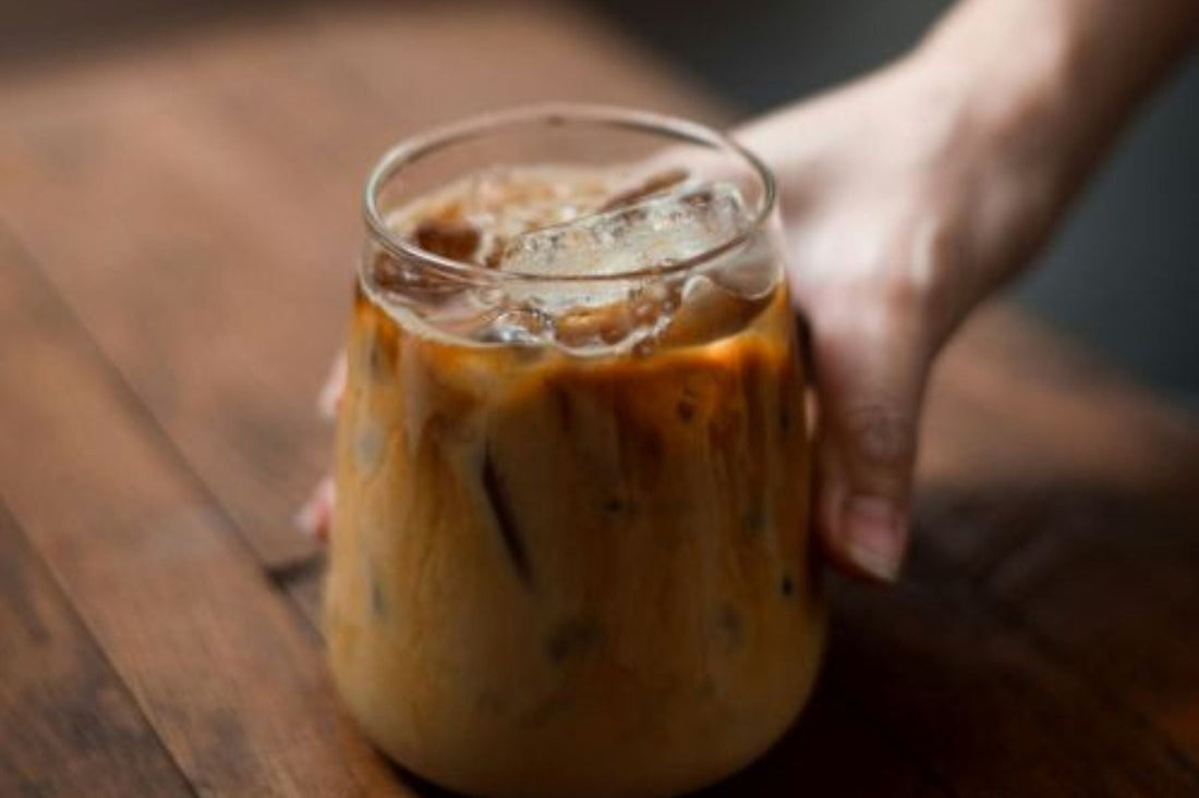 Hand holding a glass jar of Sweet Cream Iced Chai Latte on a wooden table