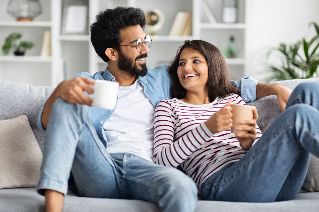 Couple relaxing on a couch, smiling and drinking tea together