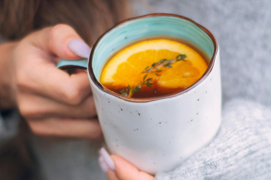 A person holding a cup of Orange Pekoe Tea with orange slices in it