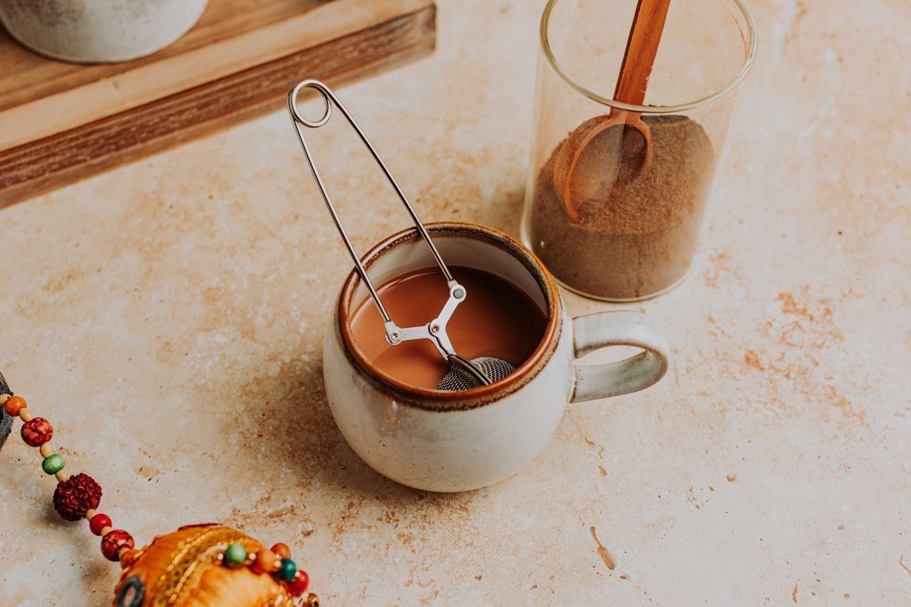 Infuser steeping in a mug of milky chai tea near a jar of loose tea.
