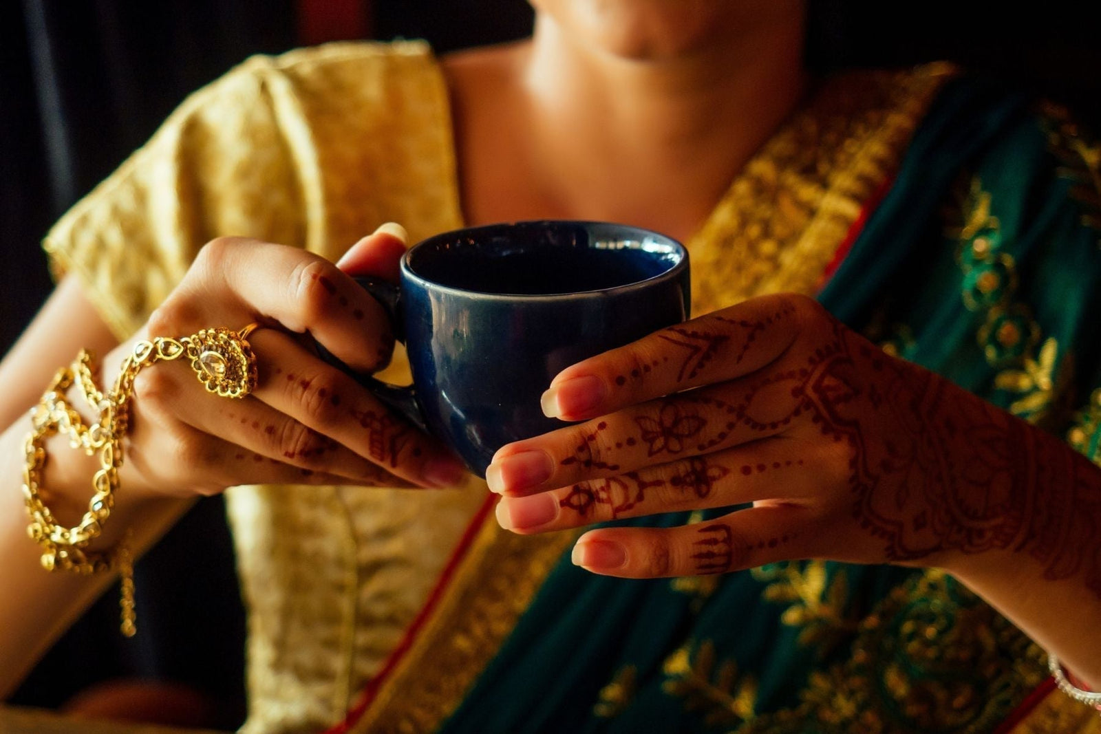 A woman wearing a saree holding a cup on her hands