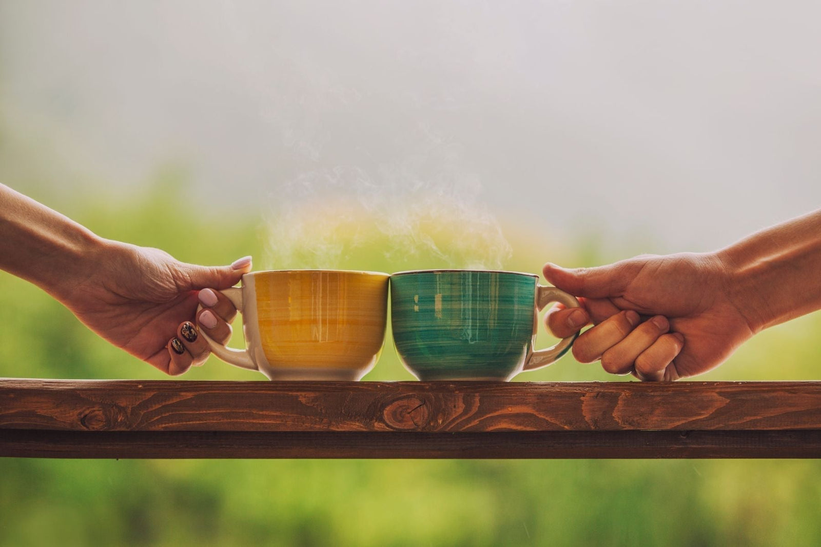 Two hands holding yellow and green cups of hot tea outdoors