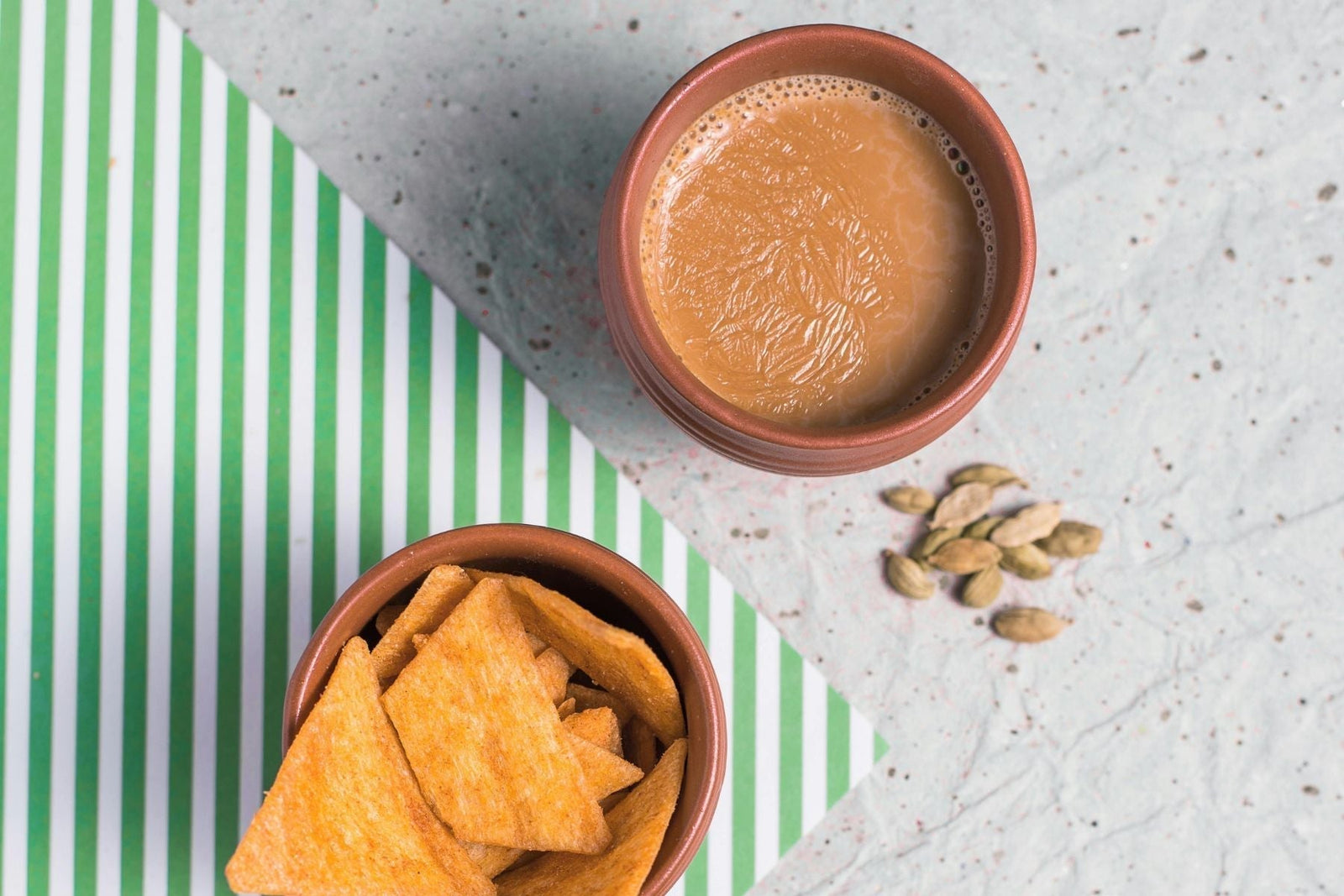Clay cup of masala chai with snacks and cardamom pods