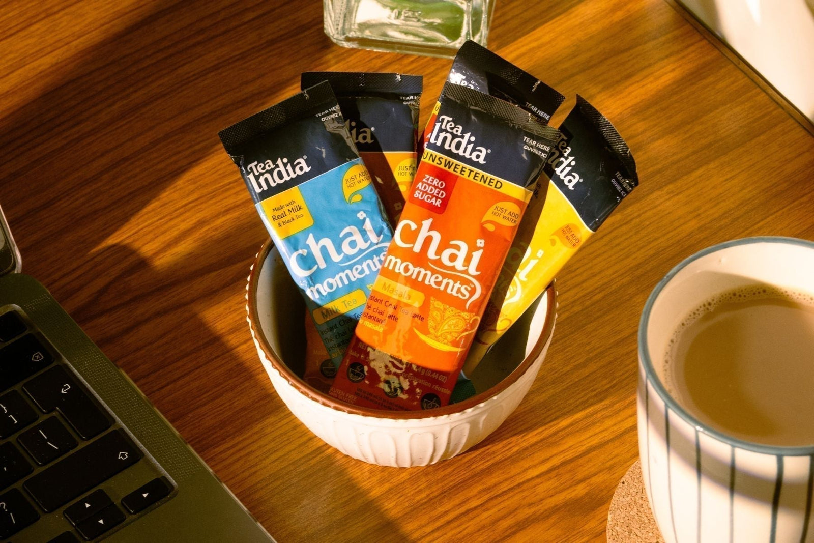 Tea India chai packets in bowl beside a cup of hot chai