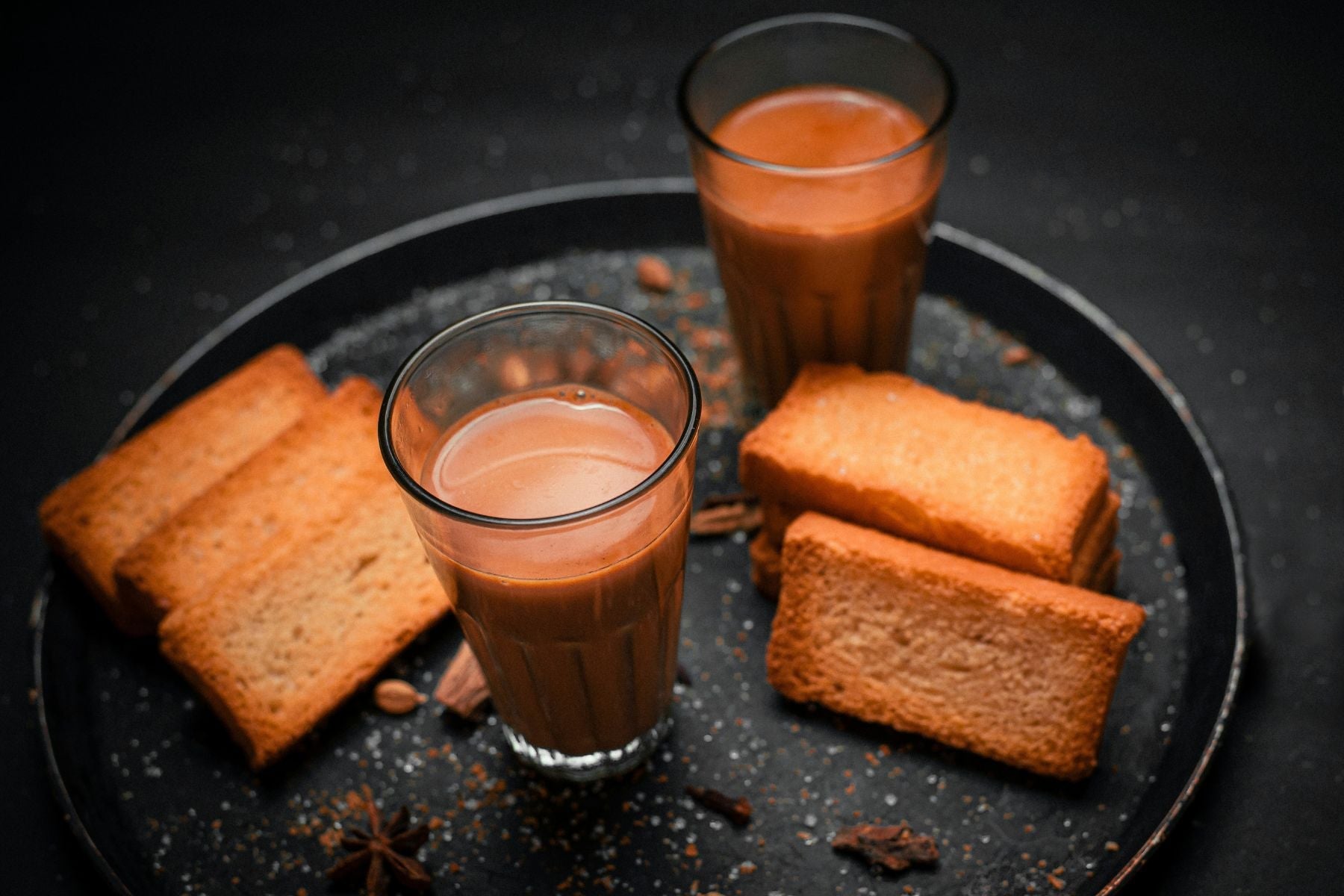 Two glasses of masala chai served with crispy rusk biscuits