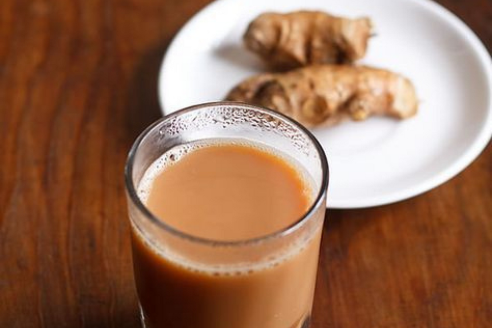 Ginger in a white plate next to glass filled with tea kept on table