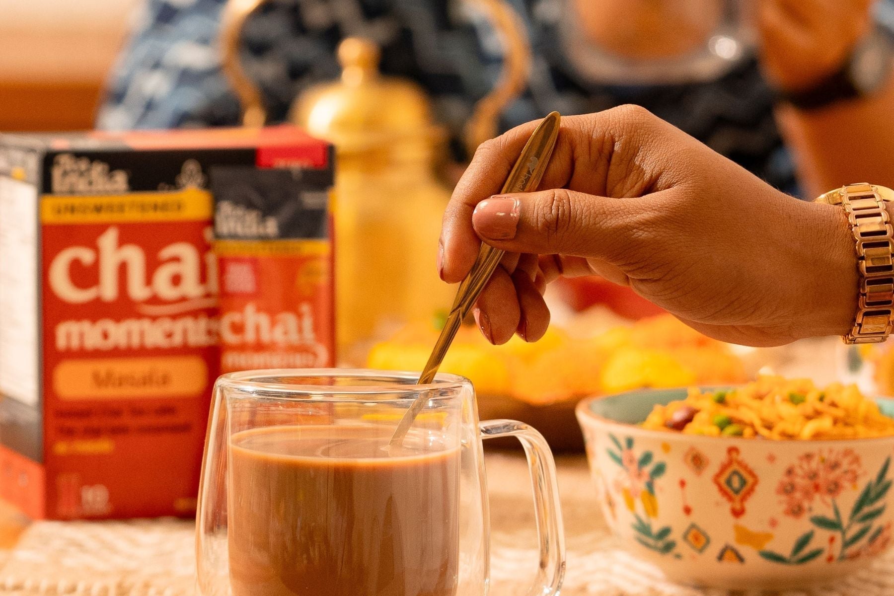 Hand stirring a glass of masala chai with Tea India packet nearby