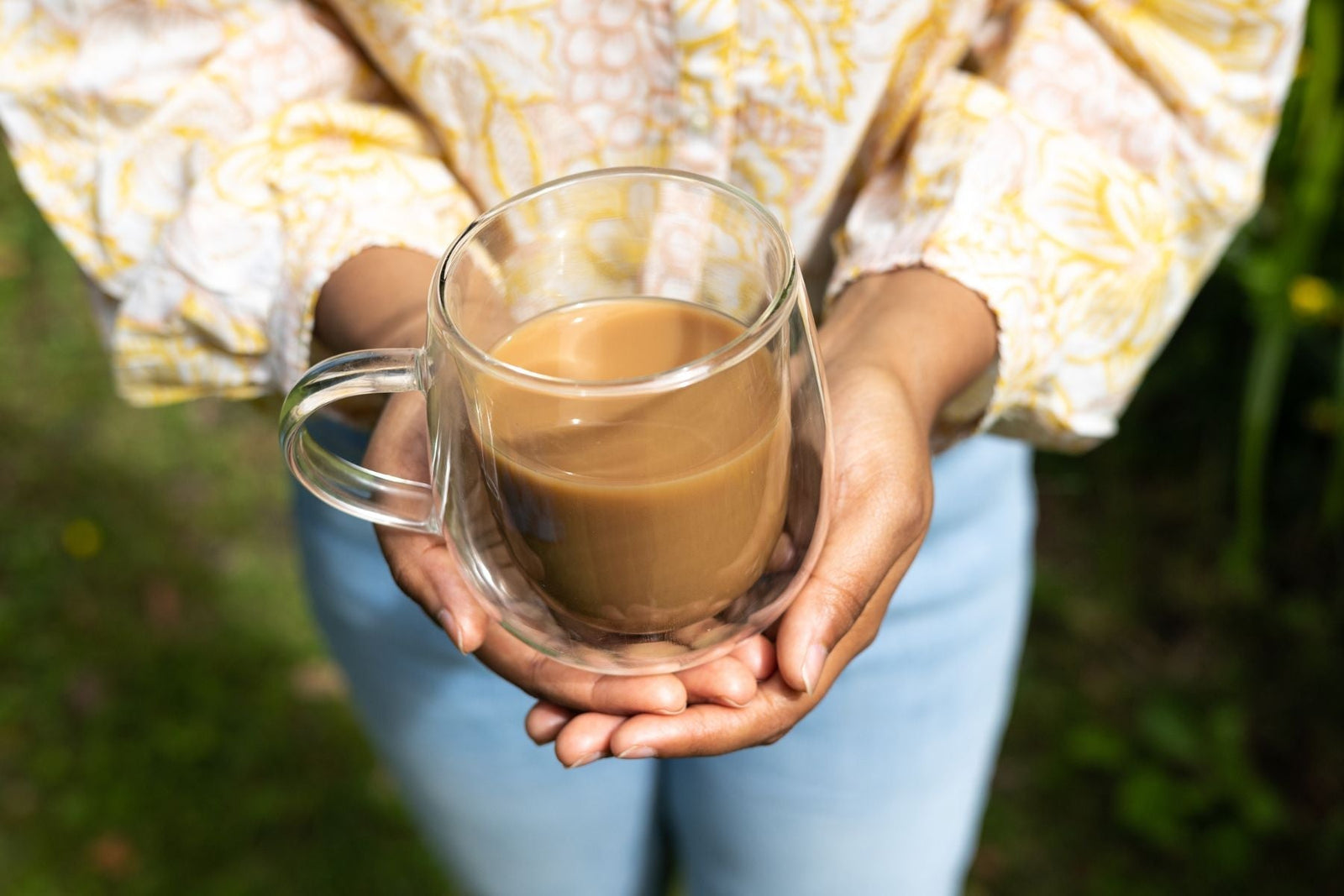 Close-up of a person holding a clear double-walled glass mug filled with milk tea or coffee.