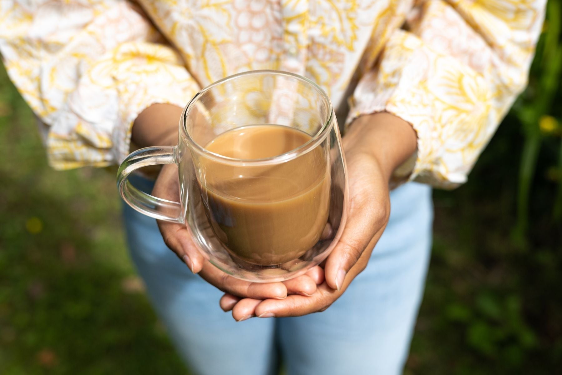 Close-up of a person holding a clear double-walled glass mug filled with milk tea or coffee.