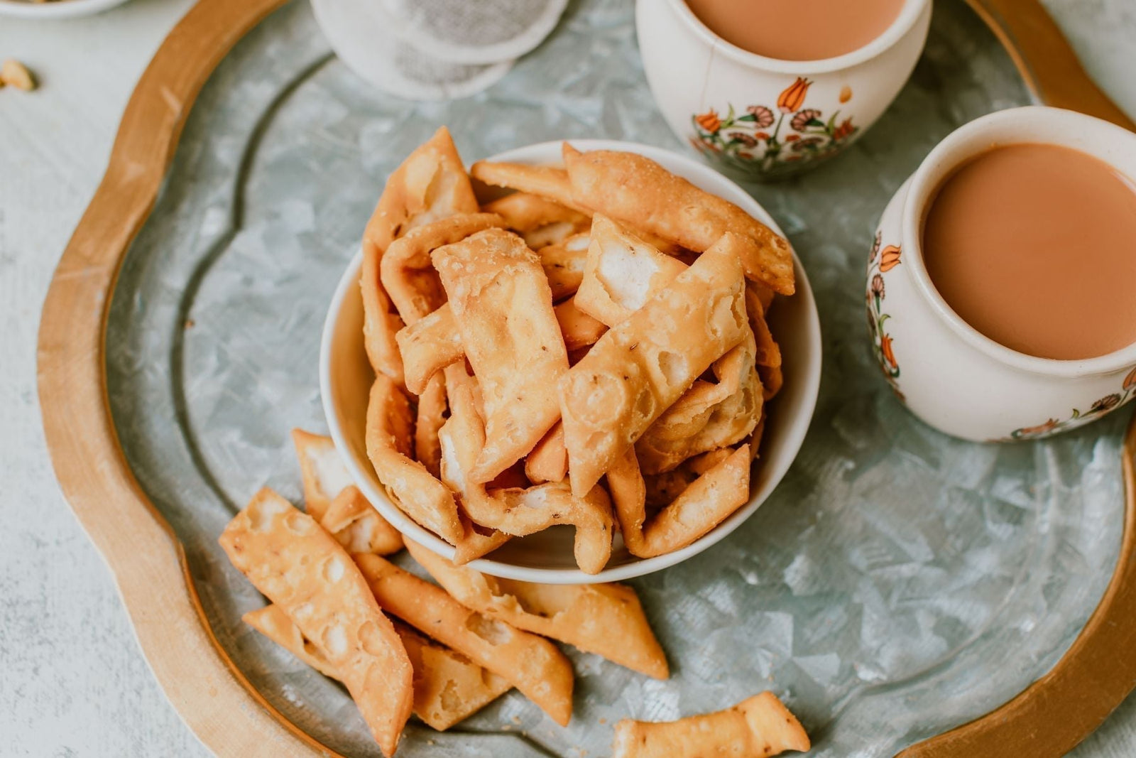 Fried savory Indian snacks (Namak Para) and chai on a tray.