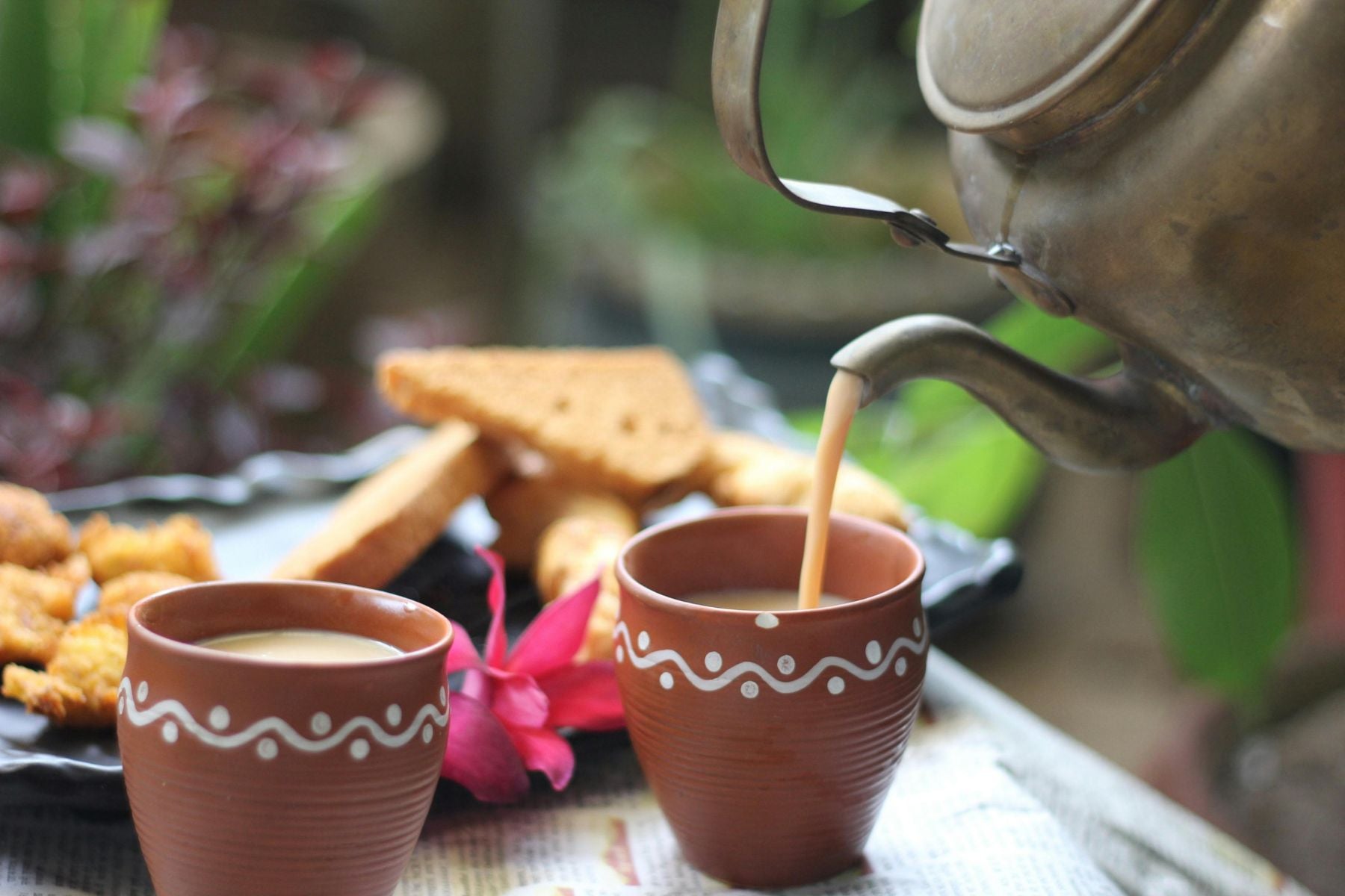 Chai pouring from a brass kettle into a clay cup.
