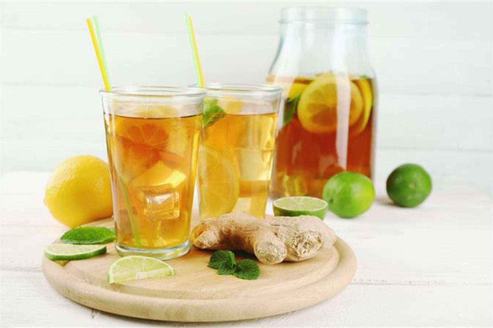 Two glasses of Iced Ginger Tea along with a pitcher of it with Ginger and lemon around