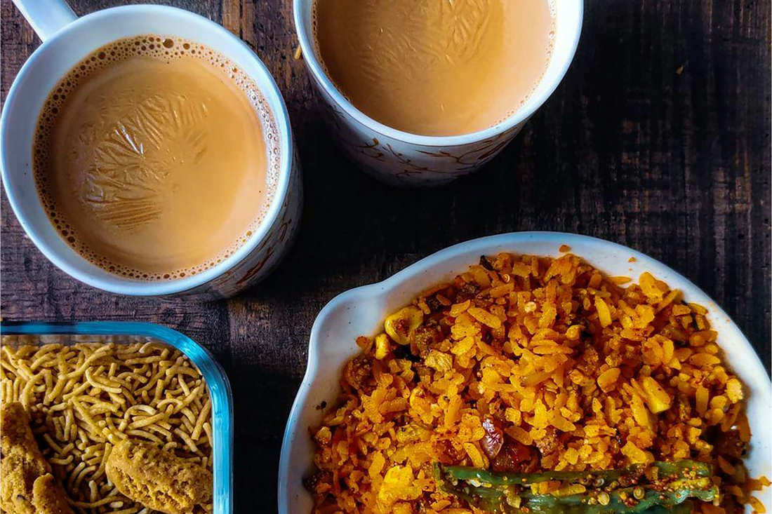 Cup of milk tea with poha and some spices in bowls kept on a table