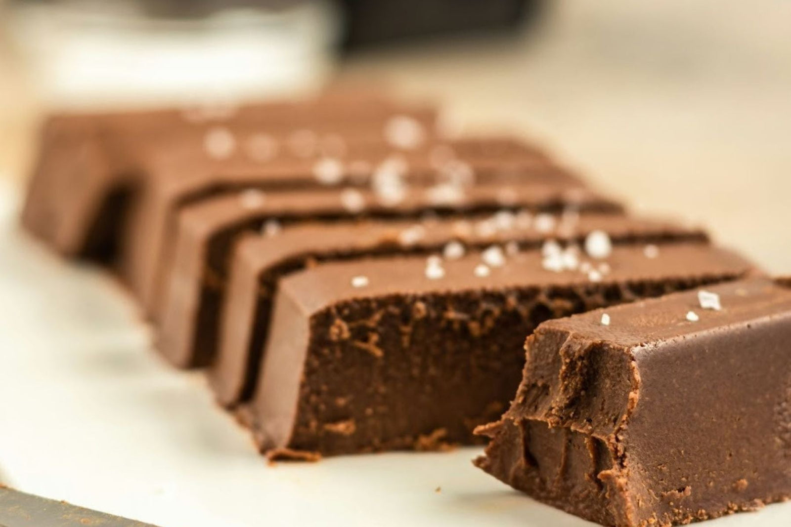 A close-up shot of several slices of rich, dark chai fudge topped with flakes of sea salt, arranged in a line.