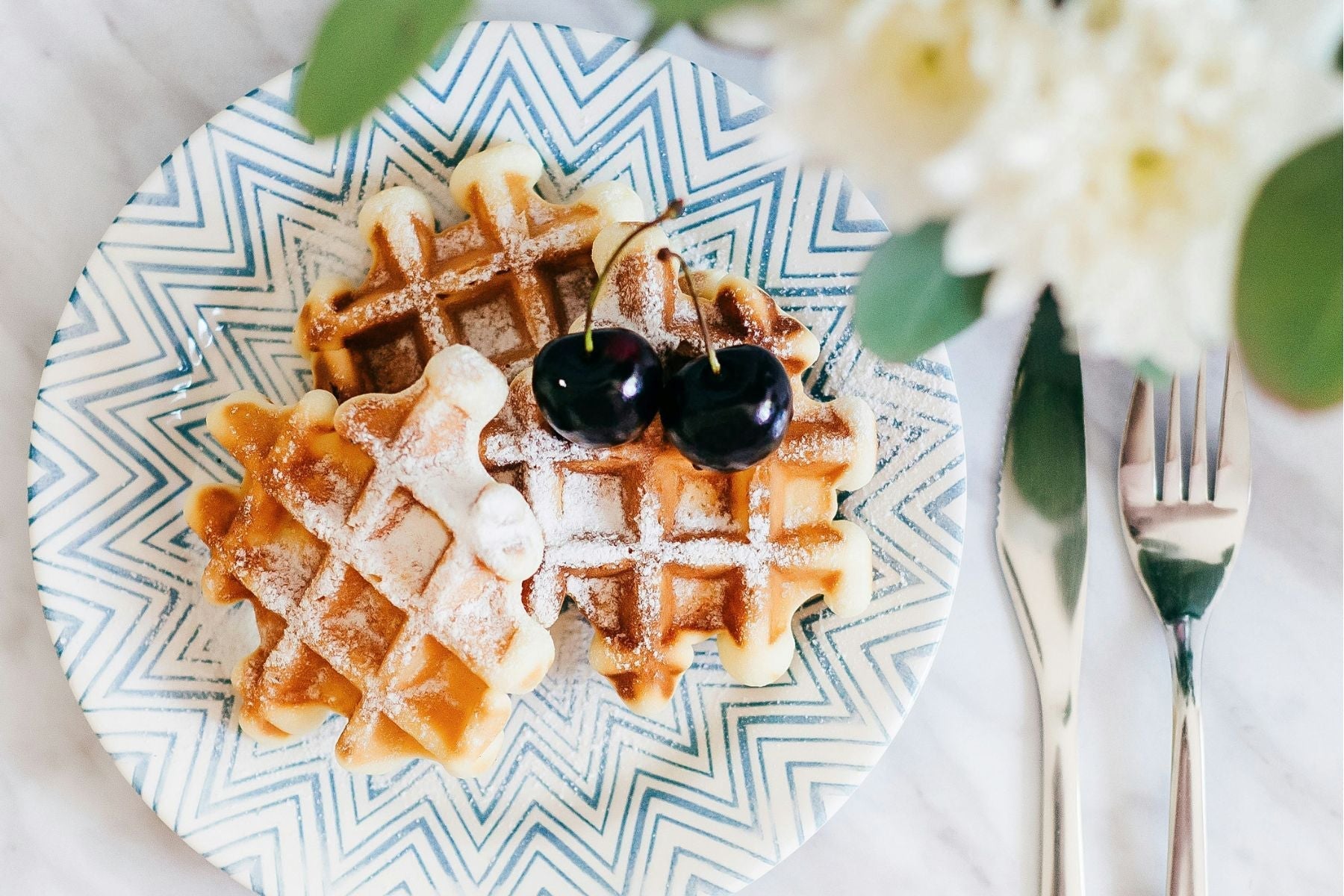 Waffles topped with cherries and powdered sugar on a patterned plate.