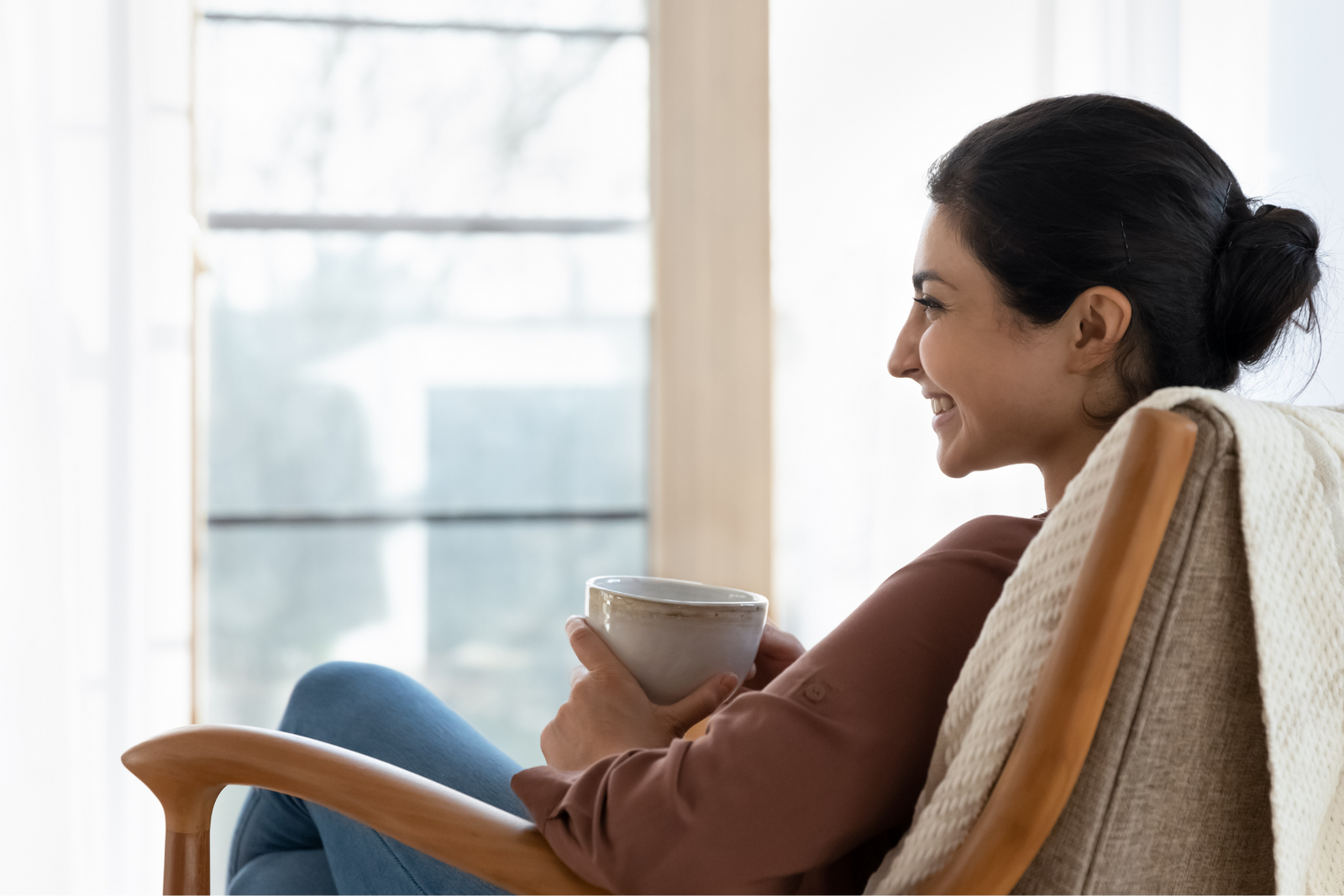 A smiling woman sitting on wooden chair holding a tea cup