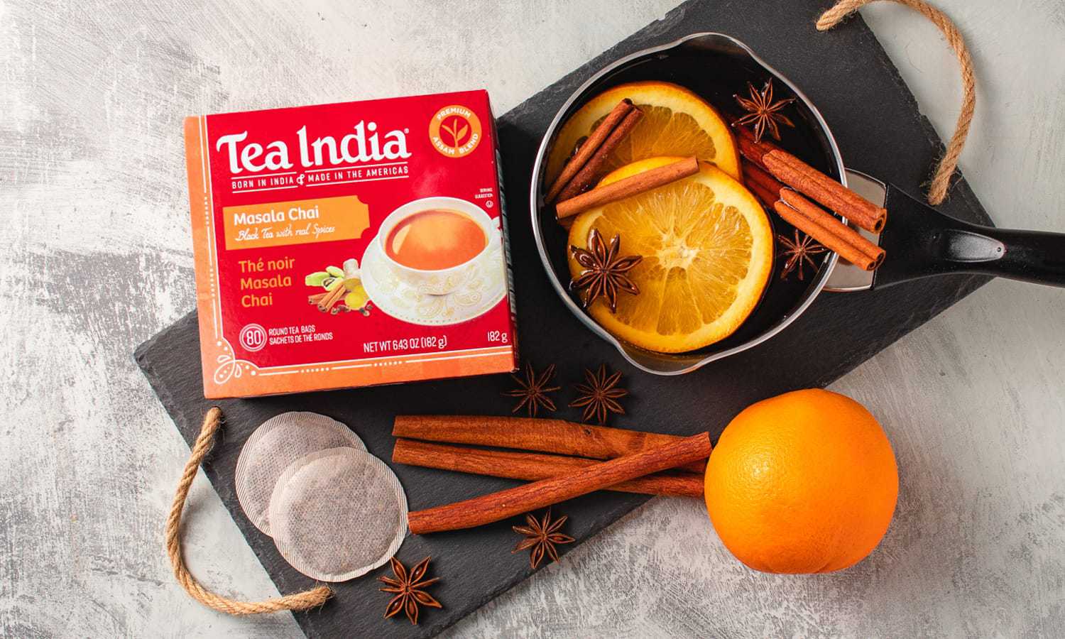 A Tea India tea bag box along with orange slices, star anise in a sauce pan