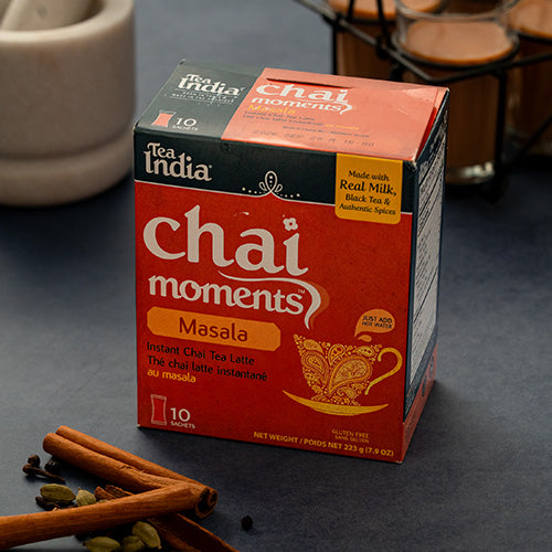 Box of Tea India Chai Moments Masala on a dark surface with cinnamon sticks and cardamom pods.