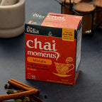 Box of Tea India Chai Moments Masala on a dark surface with cinnamon sticks and cardamom pods.
