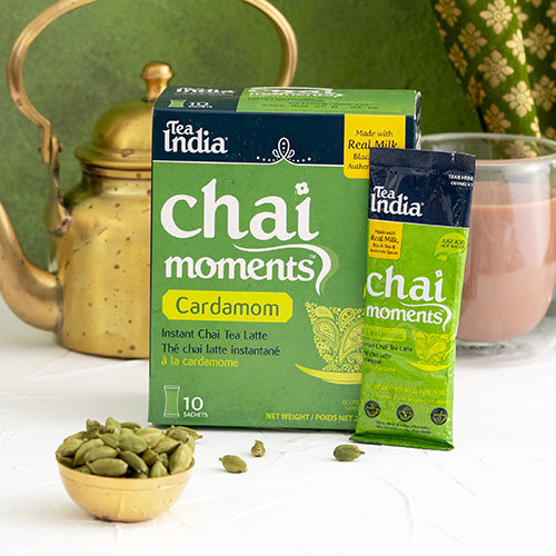 Tea India Chai Moments Cardamom packaging with a brass teapot and cardamom pods on a white surface.