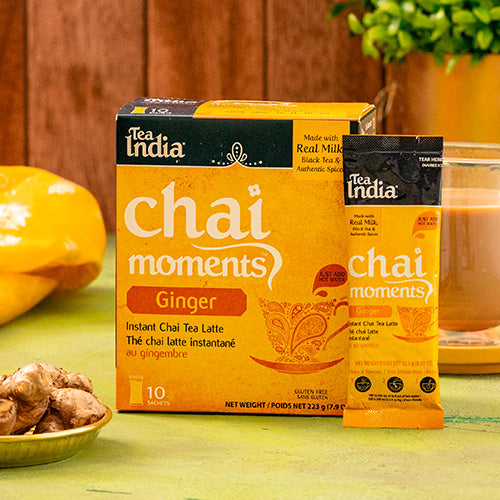 Tea India Chai Moments Ginger instant chai tea latte packaging on a green surface with a wooden background.