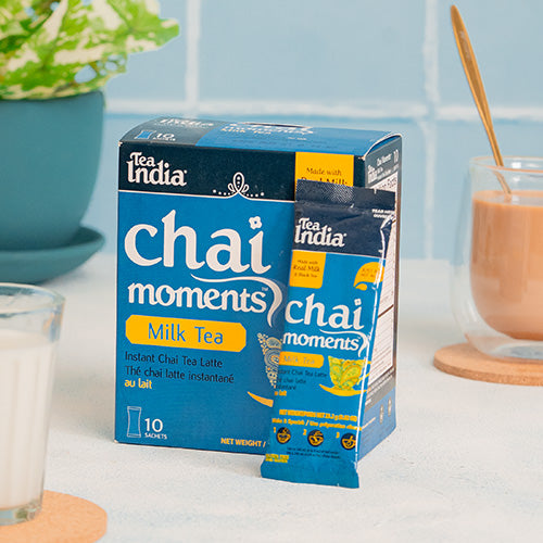 Box of Tea India Chai Moments Milk Tea on a kitchen counter with a glass of milk and a cup of tea.